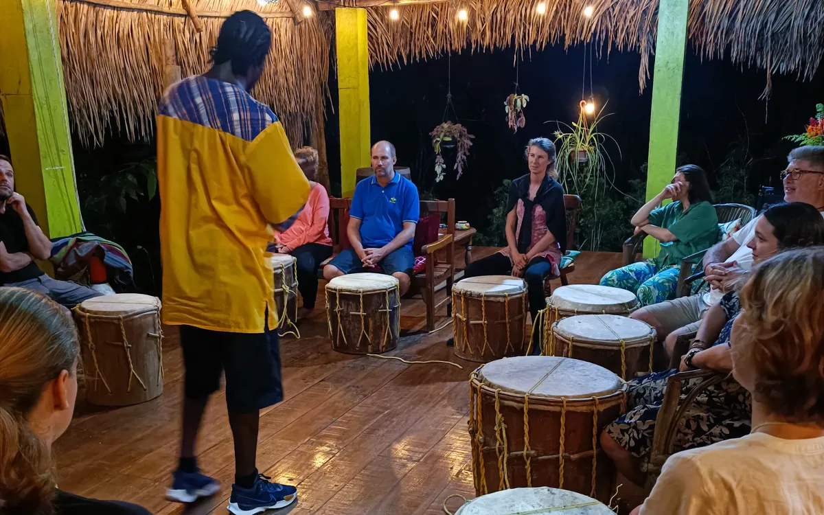 Garifuna-Trommelkreis: Gäste mit traditionellen Trommeln unter einem Palmblattdach am Abend