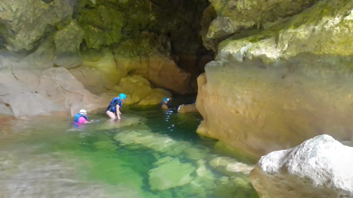 Gäste mit Helmen waten durch einen klaren Pool in einer Höhle